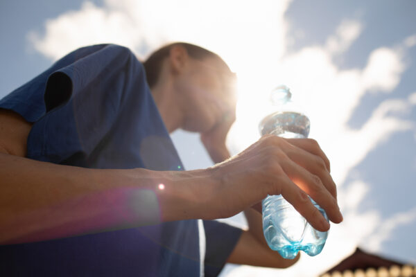 Person experiencing heat stress while holding a water bottle outdoors during hot weather, representing heat exhaustion and heat stroke.