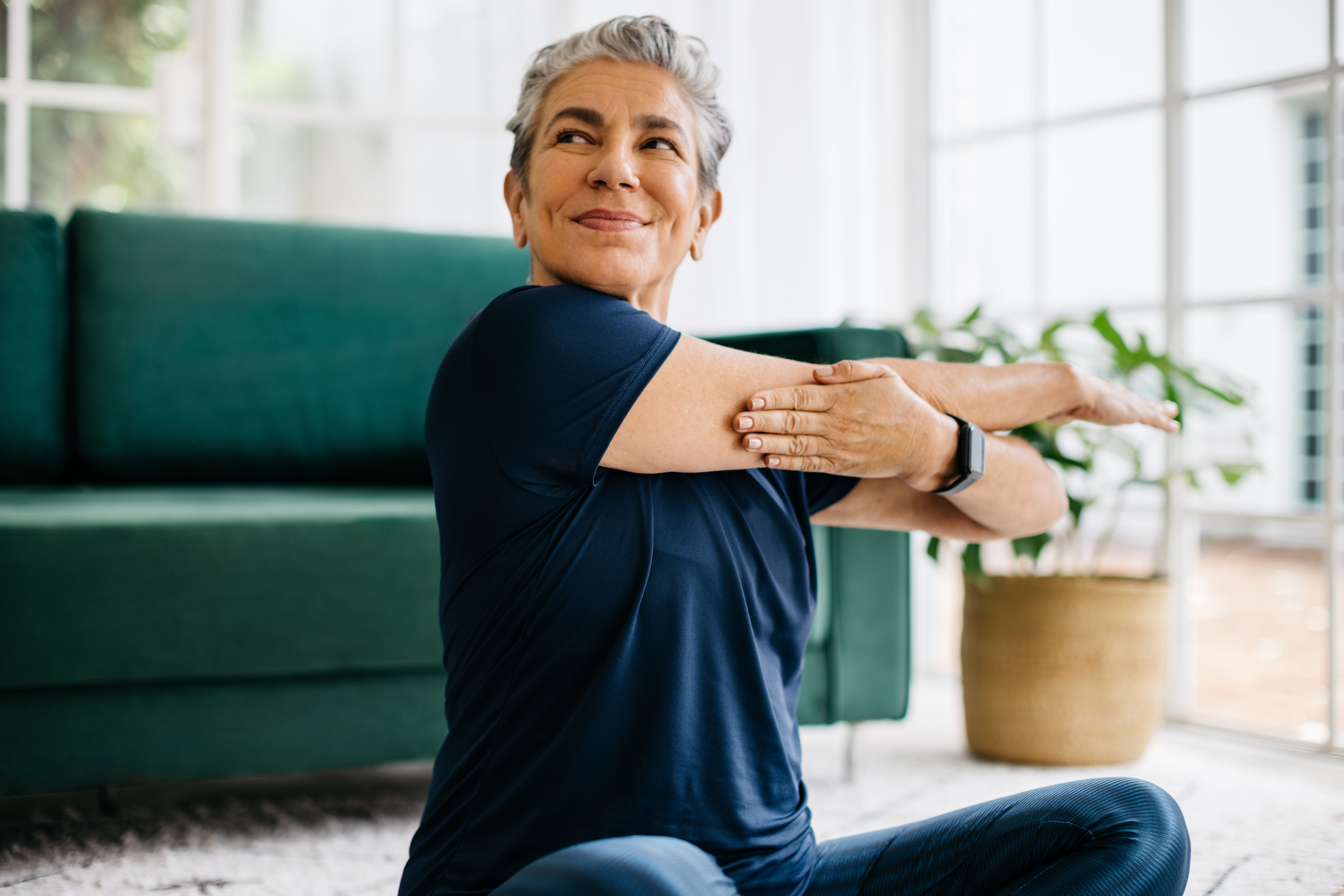 Senior self-sufficiency at home: woman doing a light stretching exercise in her living room